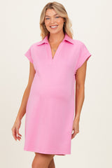 woman wearing a pink short sleeve maternity dress with a polo collar and a slightly relaxed fit, showing her baby bump