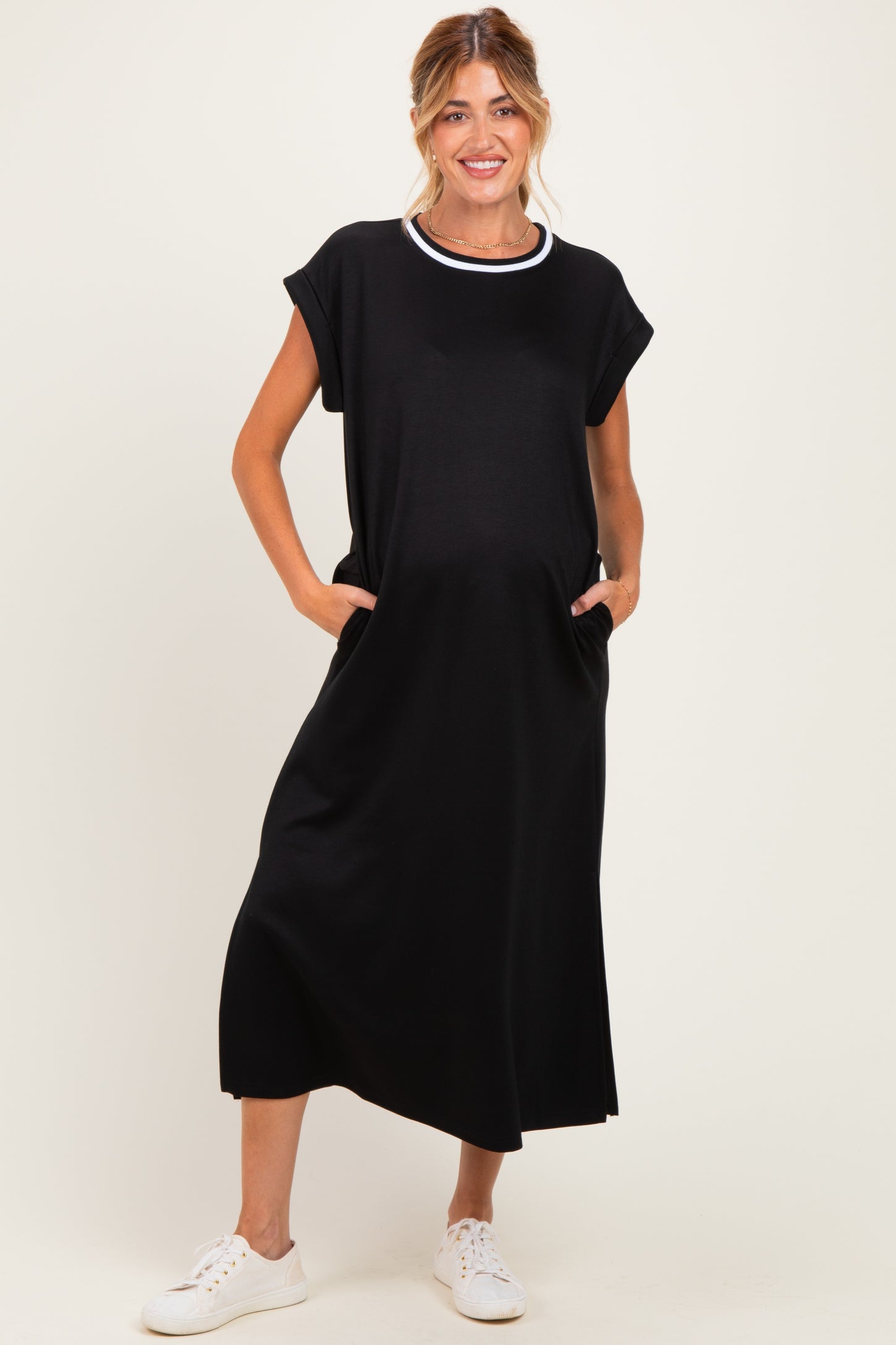woman wearing a black maternity dress with short sleeves and pockets, standing with a slight baby bump visible