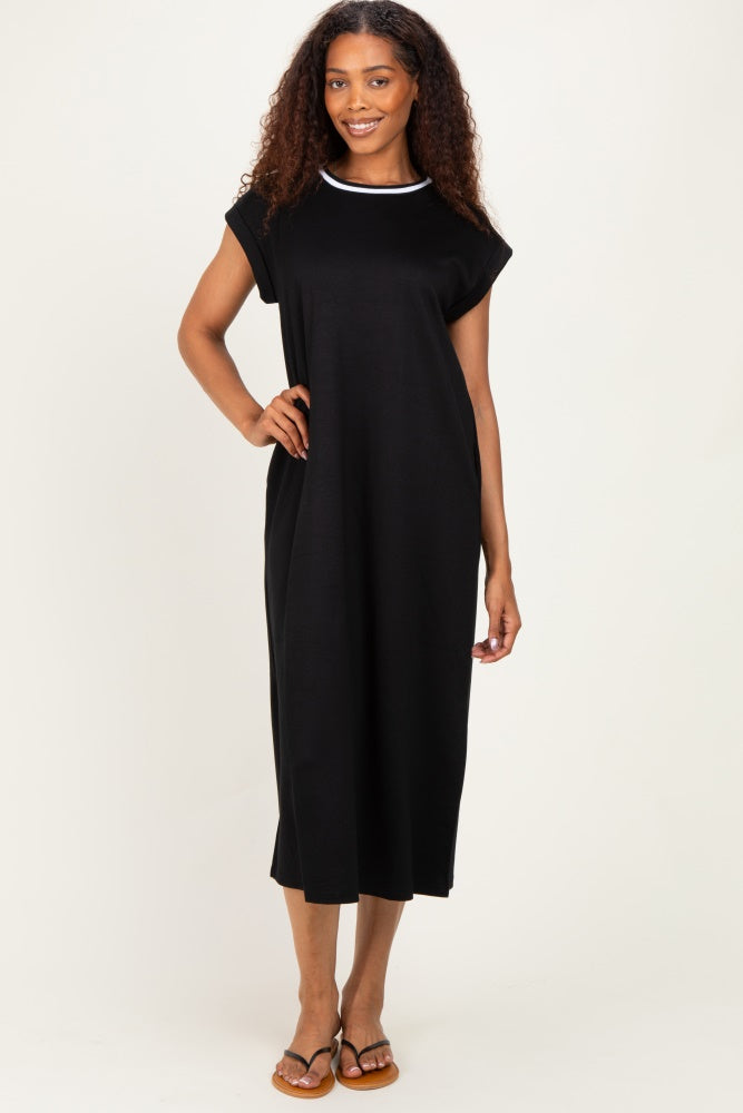 woman wearing a black midi dress with a white neckline detail, standing with one hand on her hip