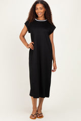 woman wearing a black midi dress with a white neckline detail, standing with one hand on her hip