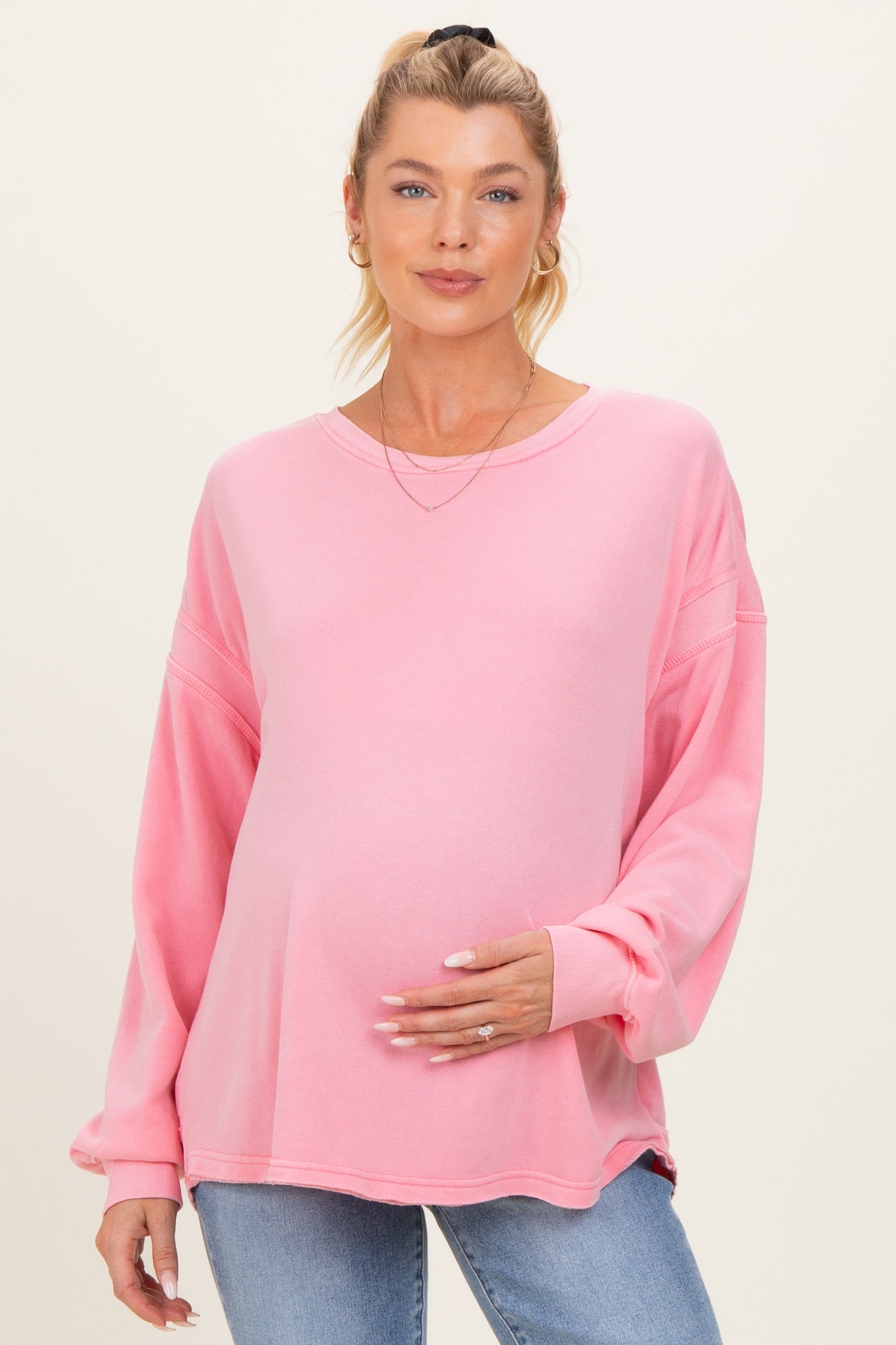 woman wearing a pink long sleeve maternity sweatshirt and holding her baby bump