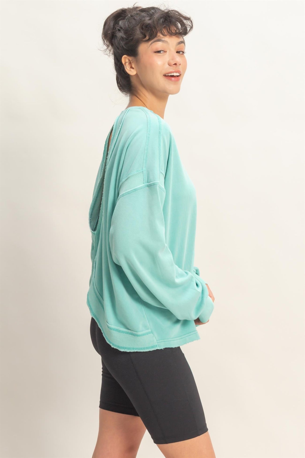 woman wearing a turquoise oversized sweatshirt with an open back and paired with black bike shorts