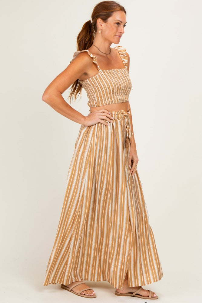 woman wearing a brown and white striped two-piece set with a crop top and maxi skirt, standing profile view