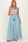 woman wearing a blue and white striped maternity two-piece set with a ruffled crop top and a maxi skirt, holding her baby bump