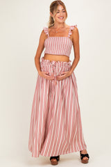 woman wearing a pink and white striped maternity two-piece set with ruffled straps and holding her baby bump