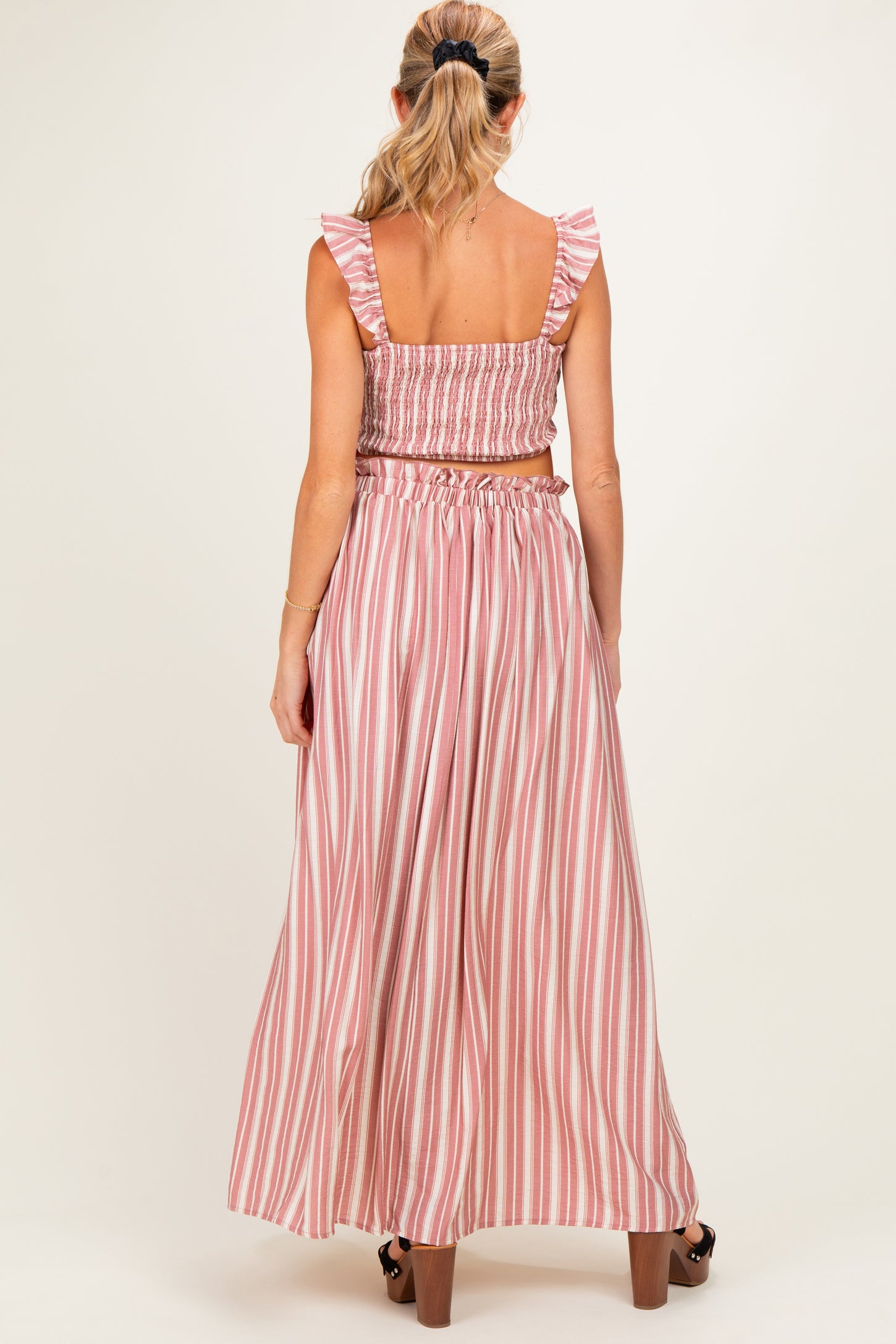 woman wearing a back view of a pink and white striped maternity two-piece set with ruffled sleeves and a flowy skirt