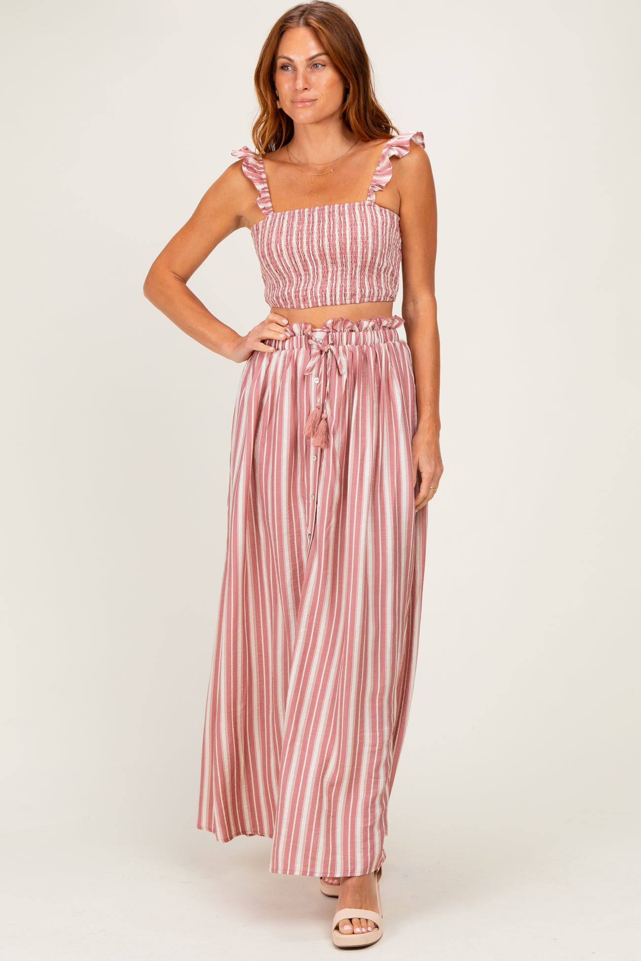 woman wearing a pink and white striped two-piece set with a smocked crop top and flowy maxi skirt