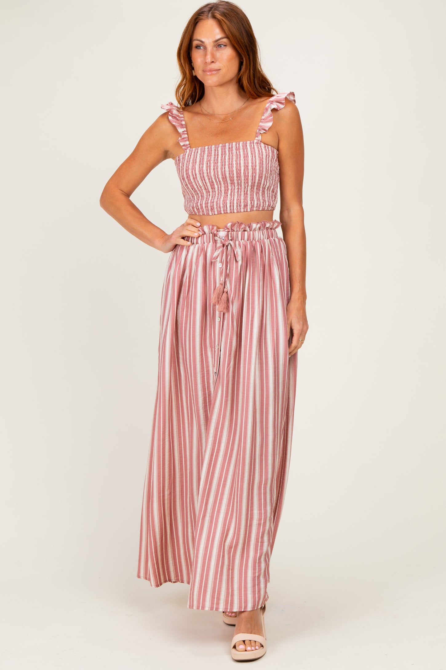 woman wearing a pink and white striped two-piece set with a smocked crop top and flowy maxi skirt
