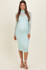 woman wearing a light mint green maternity dress with a fitted silhouette and long sheer sleeves, showing her baby bump