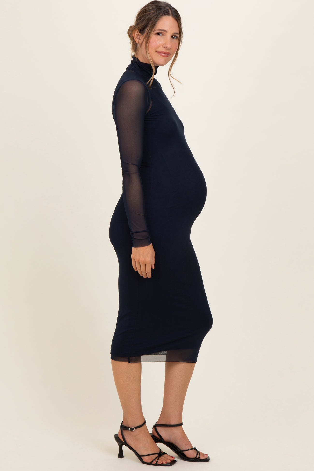woman wearing a navy long sleeve maternity dress showing her baby bump and paired with black strappy heels