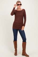 woman wearing a brown long sleeve top with ruched sides, dark blue skinny jeans, and brown knee-high boots, holding sunglasses