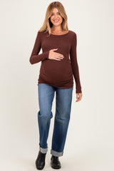 woman wearing a brown long sleeve maternity top and blue jeans, gently holding her baby bump