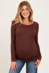 woman wearing a brown long sleeve maternity top that highlights her baby bump and paired with blue jeans