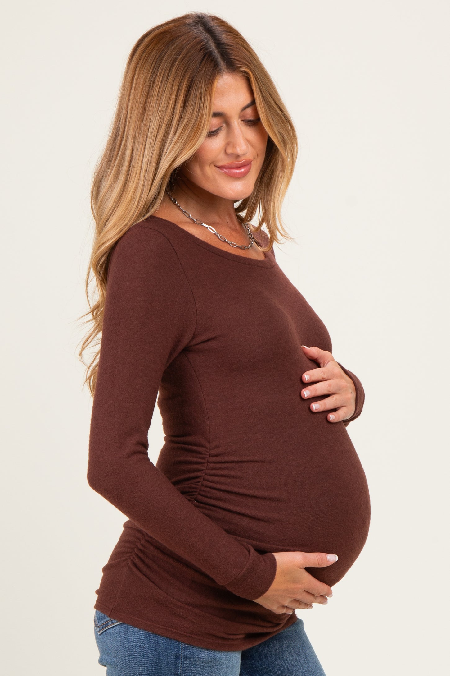 woman wearing a brown long sleeve maternity top with side ruching and holding her baby bump