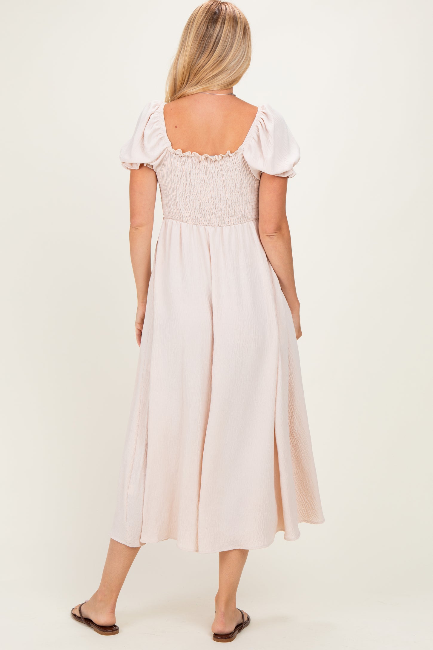 woman wearing a blush pink smocked back dress with puff sleeves, viewed from the back
