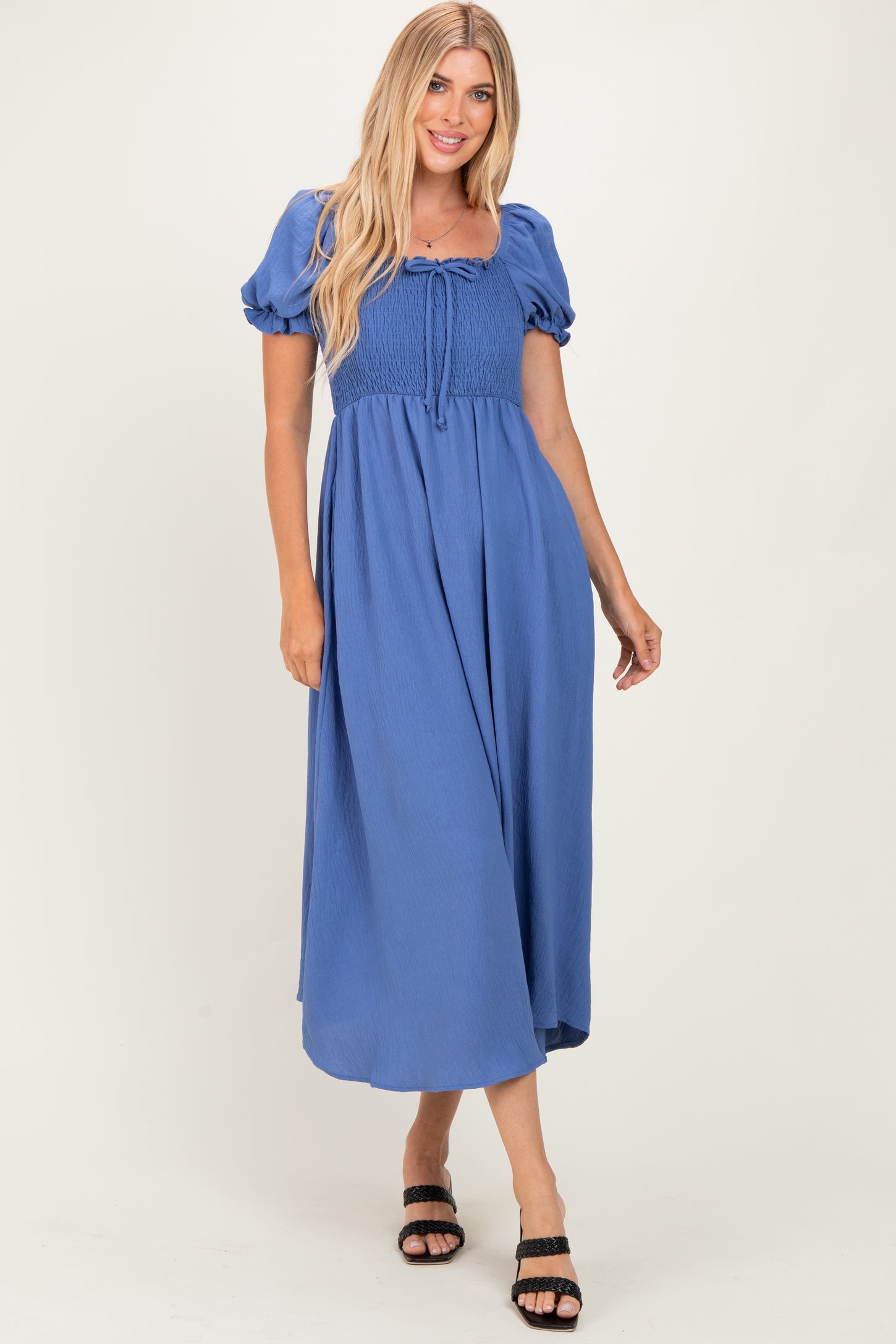 woman wearing a blue smocked maxi dress with puff sleeves and a tie detail at the neckline