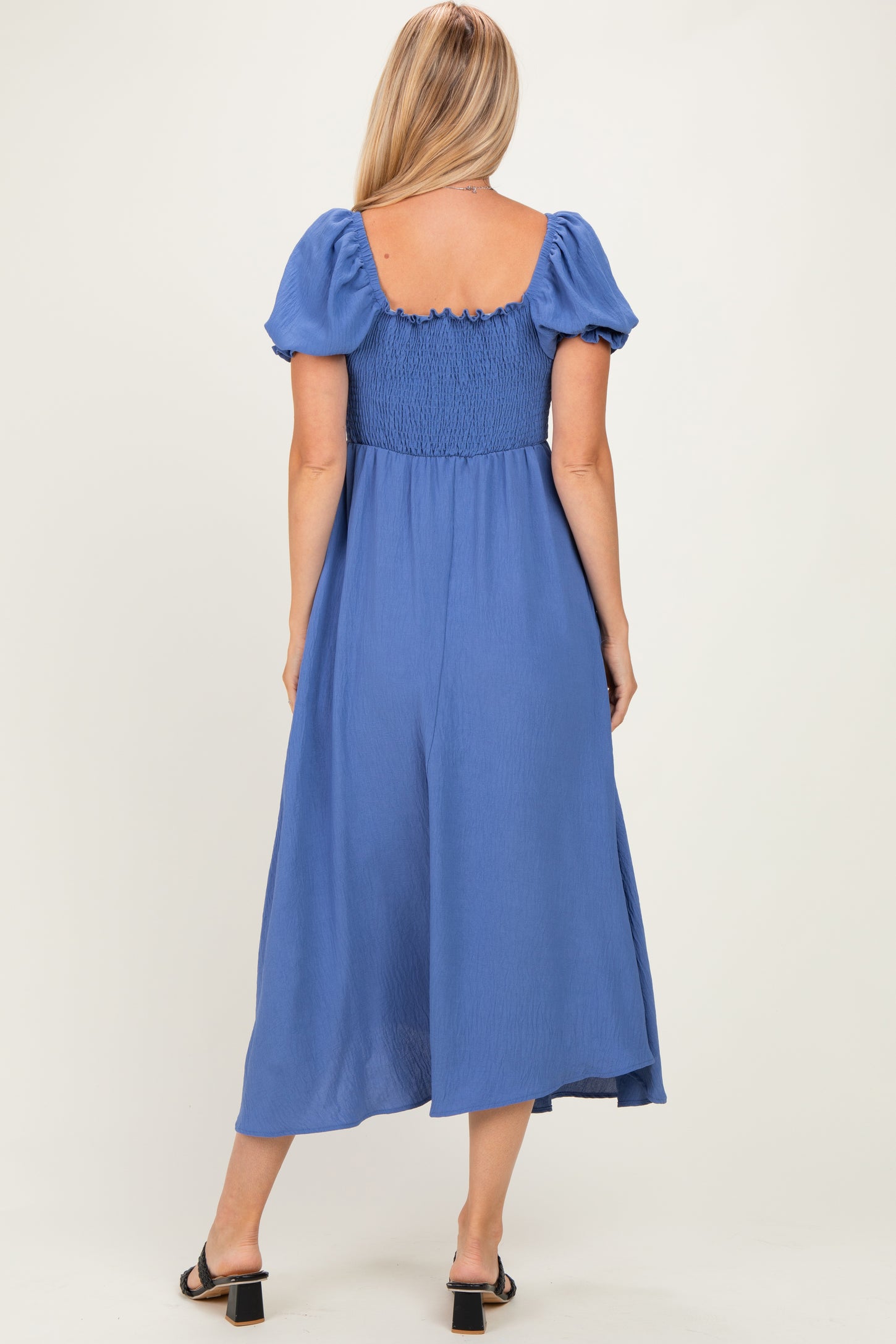woman wearing a blue midi dress with puff sleeves and a smocked back, standing with her back to the camera
