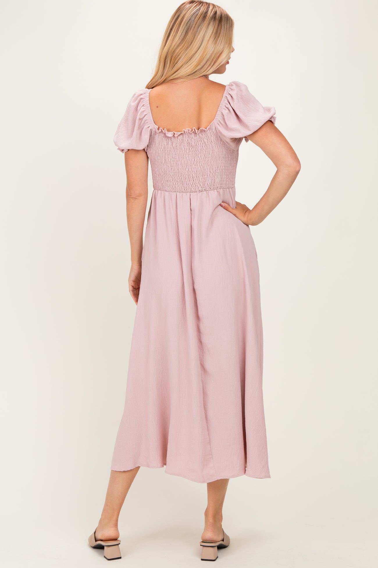 woman wearing a back view of a blush pink maxi dress with puff sleeves and a smocked bodice