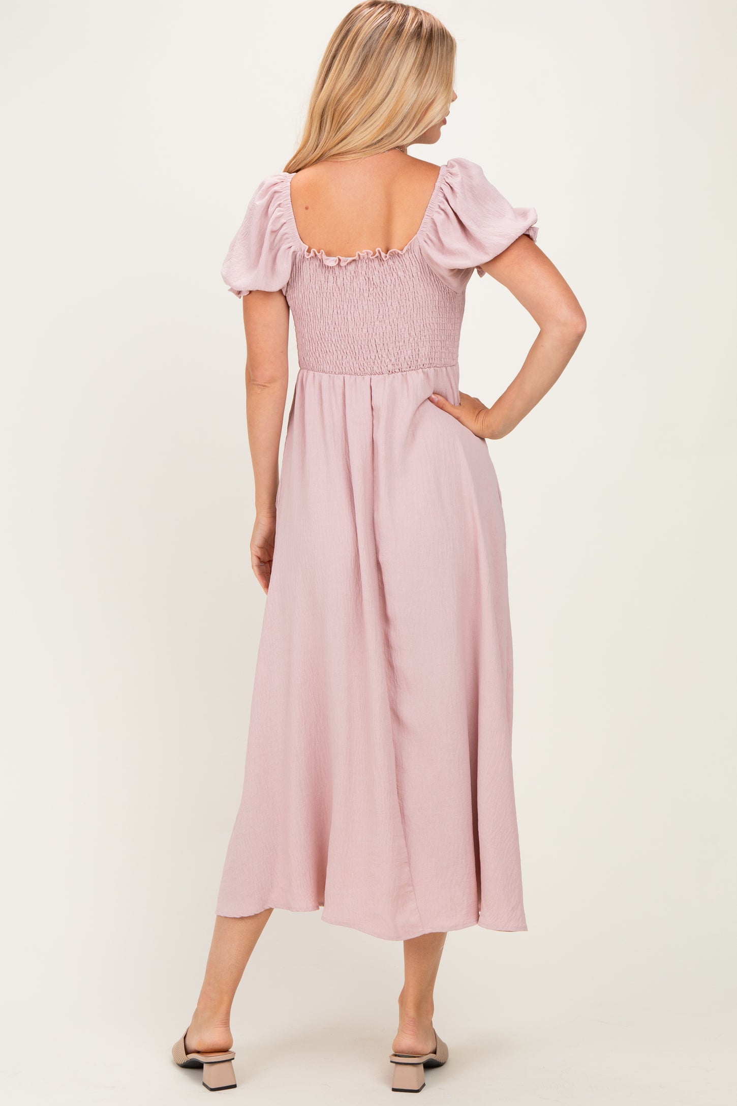 woman wearing a back view of a blush pink maxi dress with puff sleeves and a smocked bodice