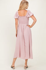 woman wearing a back view of a blush pink maxi dress with puff sleeves and a smocked bodice