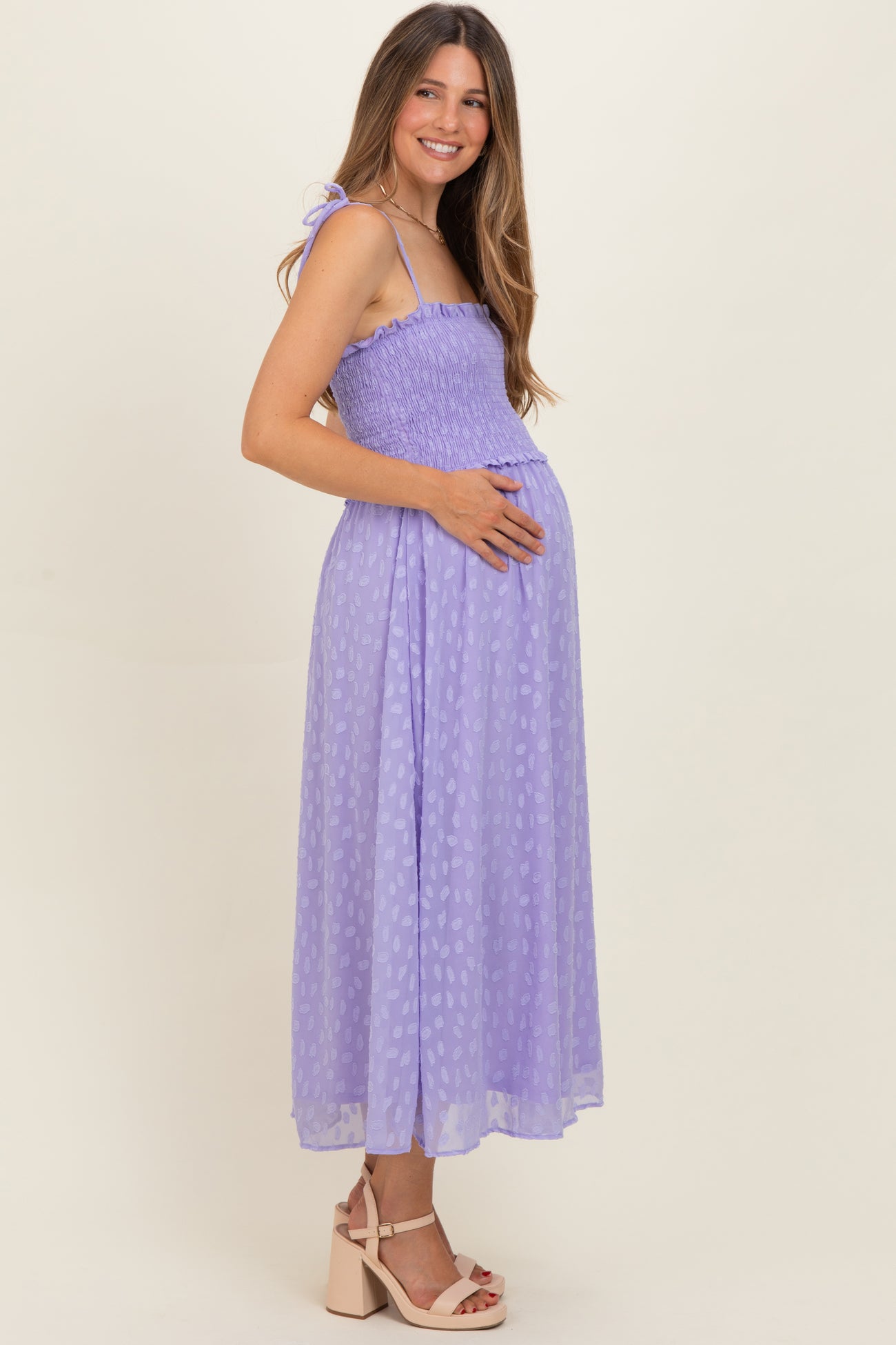 woman wearing a lavender maternity dress with smocking detail and a baby bump, standing sideways