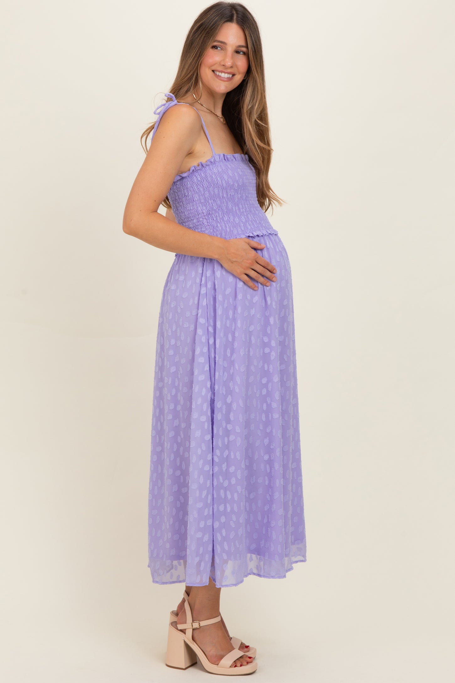 woman wearing a lavender maternity dress with smocking detail and a baby bump, standing sideways