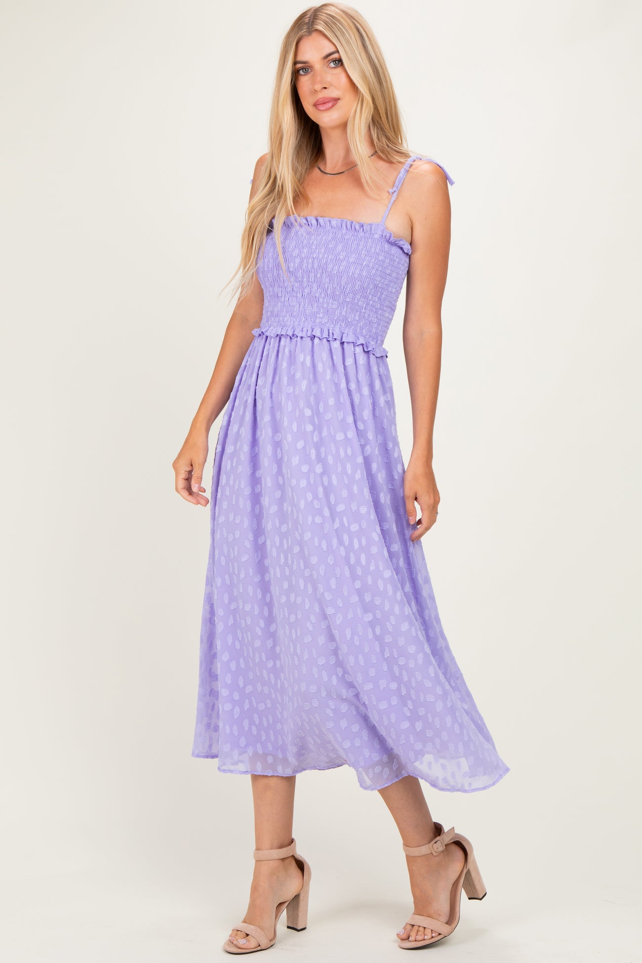 woman wearing a lavender midi dress with smocked bodice and adjustable straps, standing in a relaxed pose