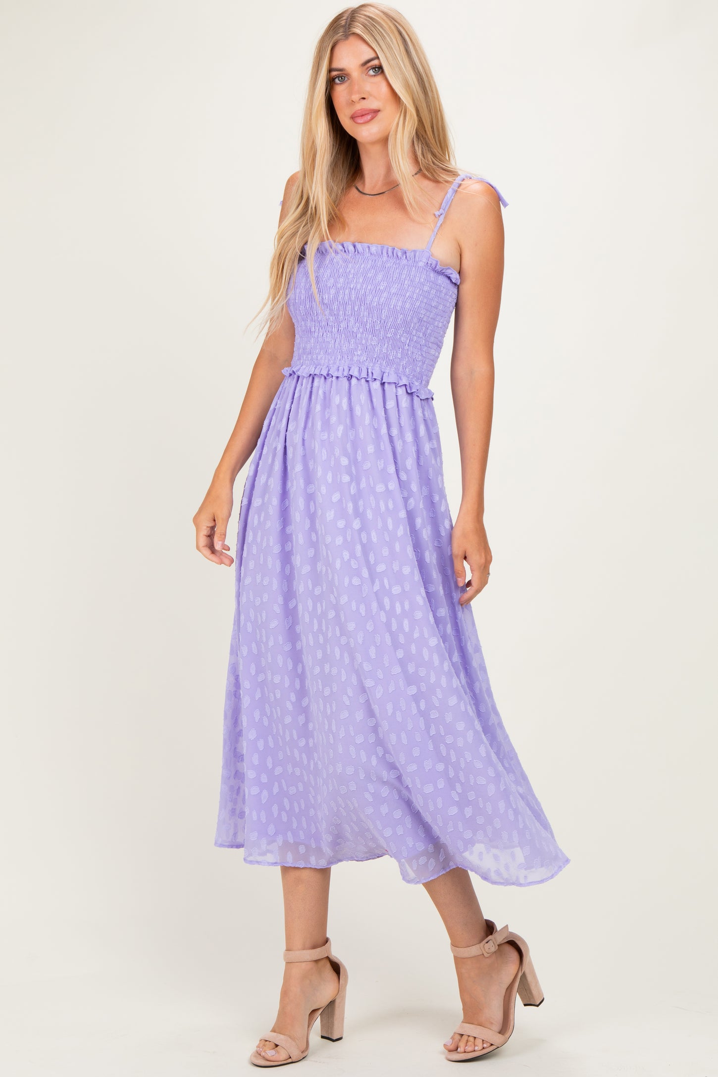 woman wearing a lavender midi dress with smocked bodice and adjustable straps, standing in a relaxed pose