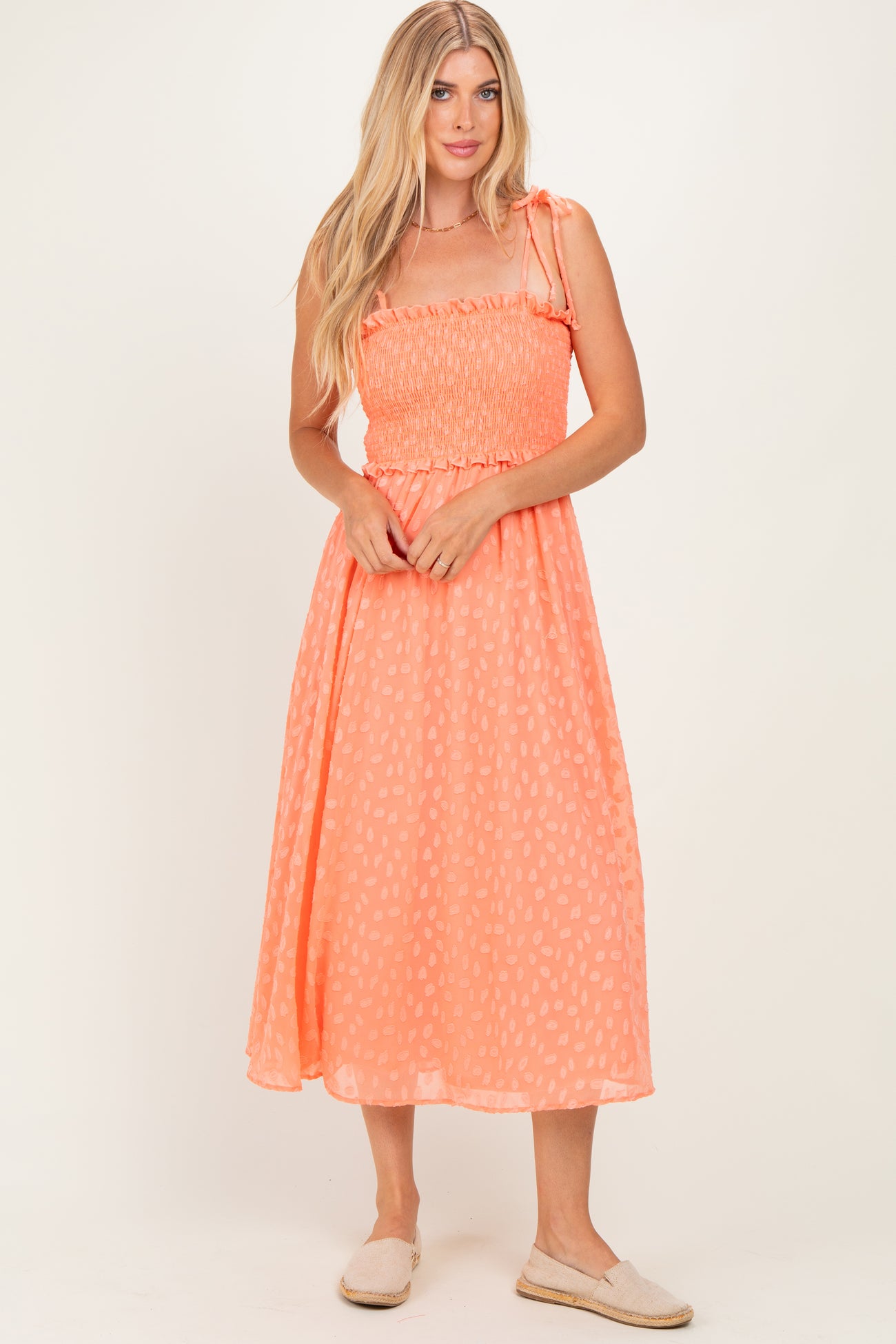 woman wearing a coral midi sundress with a smocked bodice and adjustable shoulder straps