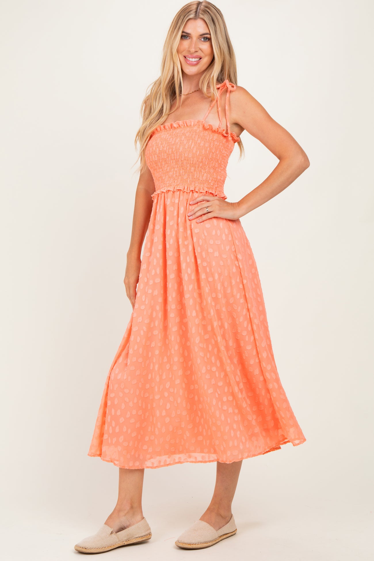 woman wearing an orange smocked midi dress with tie straps and a flowy skirt