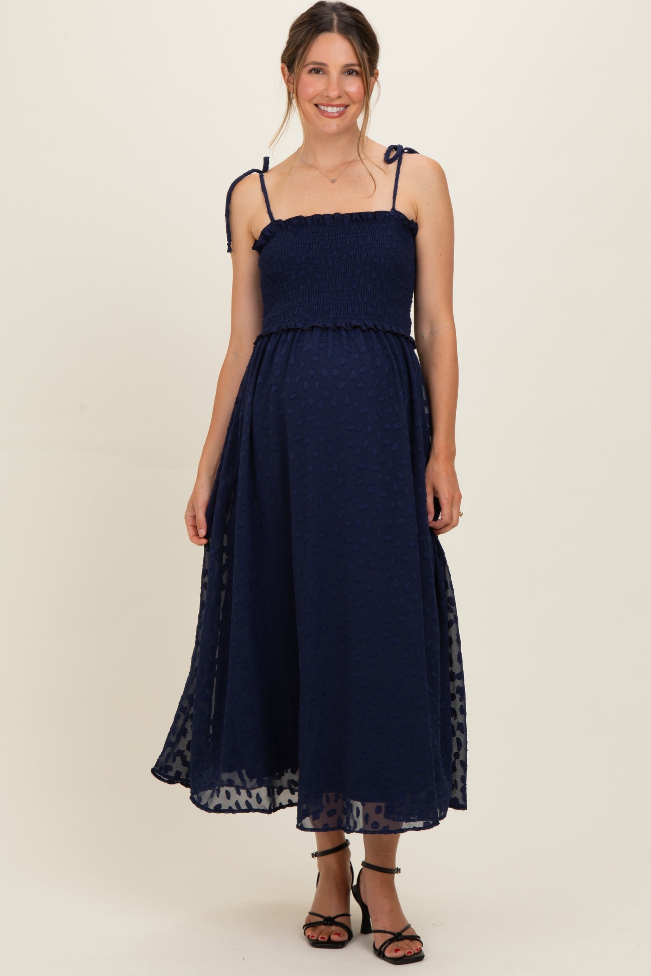 woman wearing a navy blue maternity dress with smocked bodice and adjustable straps, showcasing her baby bump