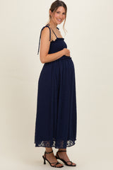 woman wearing a navy blue maternity dress with smocked bodice and tie straps, showing her baby bump
