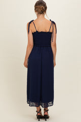 woman wearing a navy blue maternity jumpsuit with adjustable tie straps and a smocked bodice, showing a baby bump