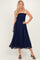 woman wearing a navy blue smocked dress with a flowy skirt and thin straps, standing in a relaxed pose