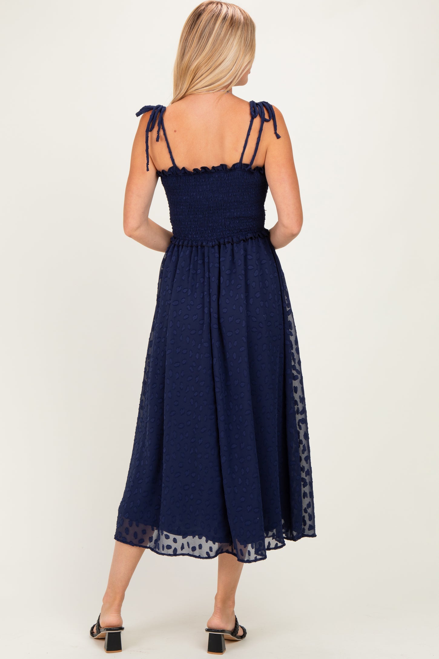woman wearing a navy blue midi dress with smocked bodice and adjustable tie straps, viewed from the back