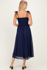 woman wearing a navy blue midi dress with smocked bodice and adjustable tie straps, viewed from the back