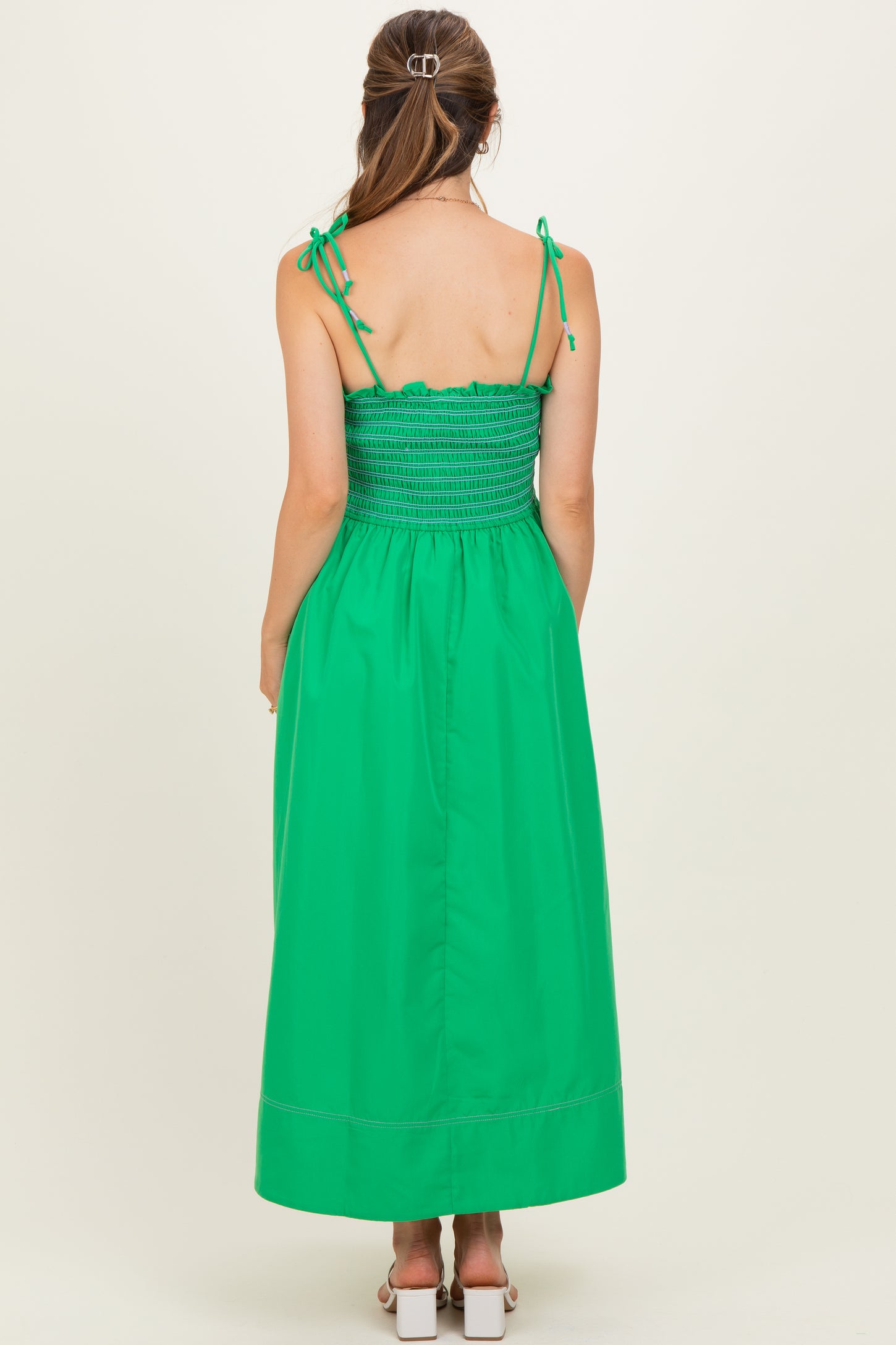woman wearing a green smocked maternity dress with adjustable straps and a flowy maxi length