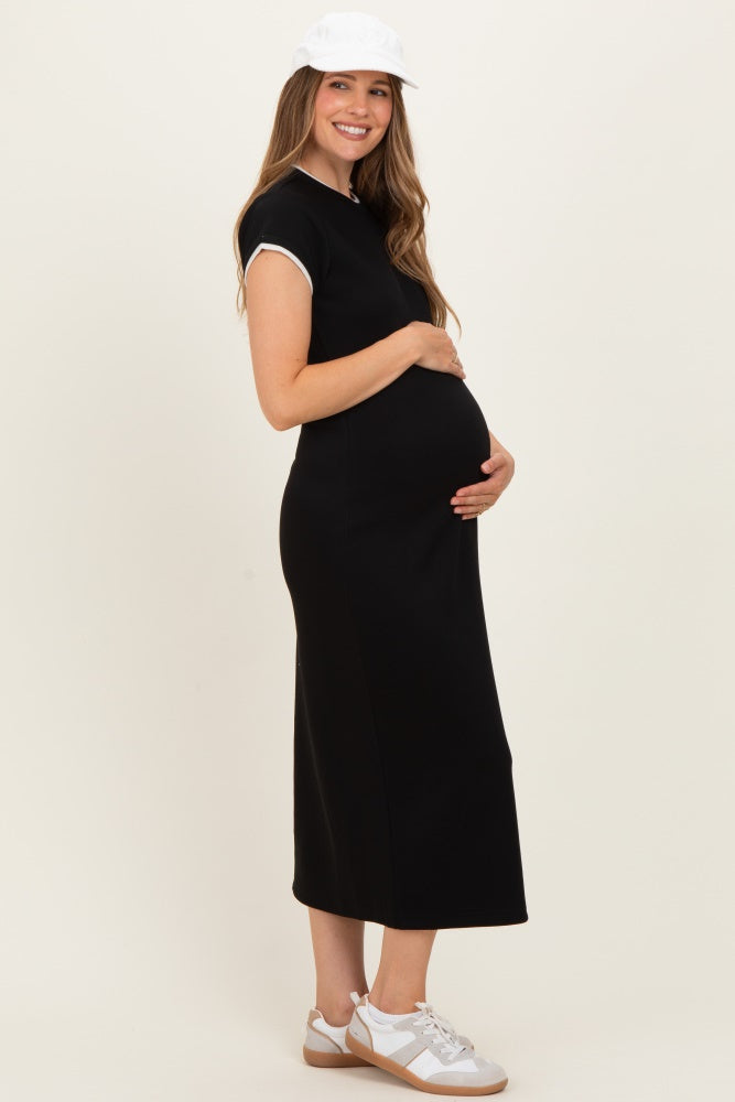 woman wearing a black maternity dress with short sleeves, holding her baby bump, and wearing a white cap