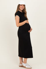woman wearing a black maternity dress with short sleeves, holding her baby bump, and wearing a white cap