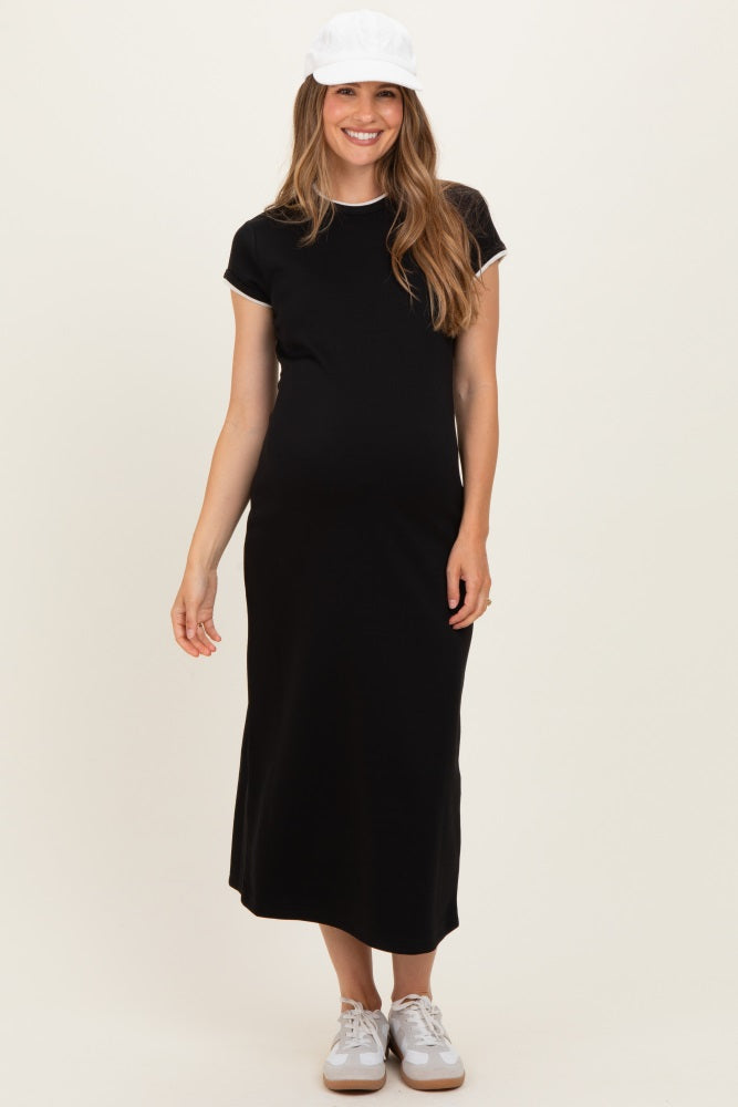 woman wearing a black maternity dress with short sleeves and white trim, standing and showing her baby bump