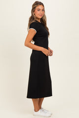 woman wearing a black midi dress with short sleeves and white trim, standing sideways with a neutral background
