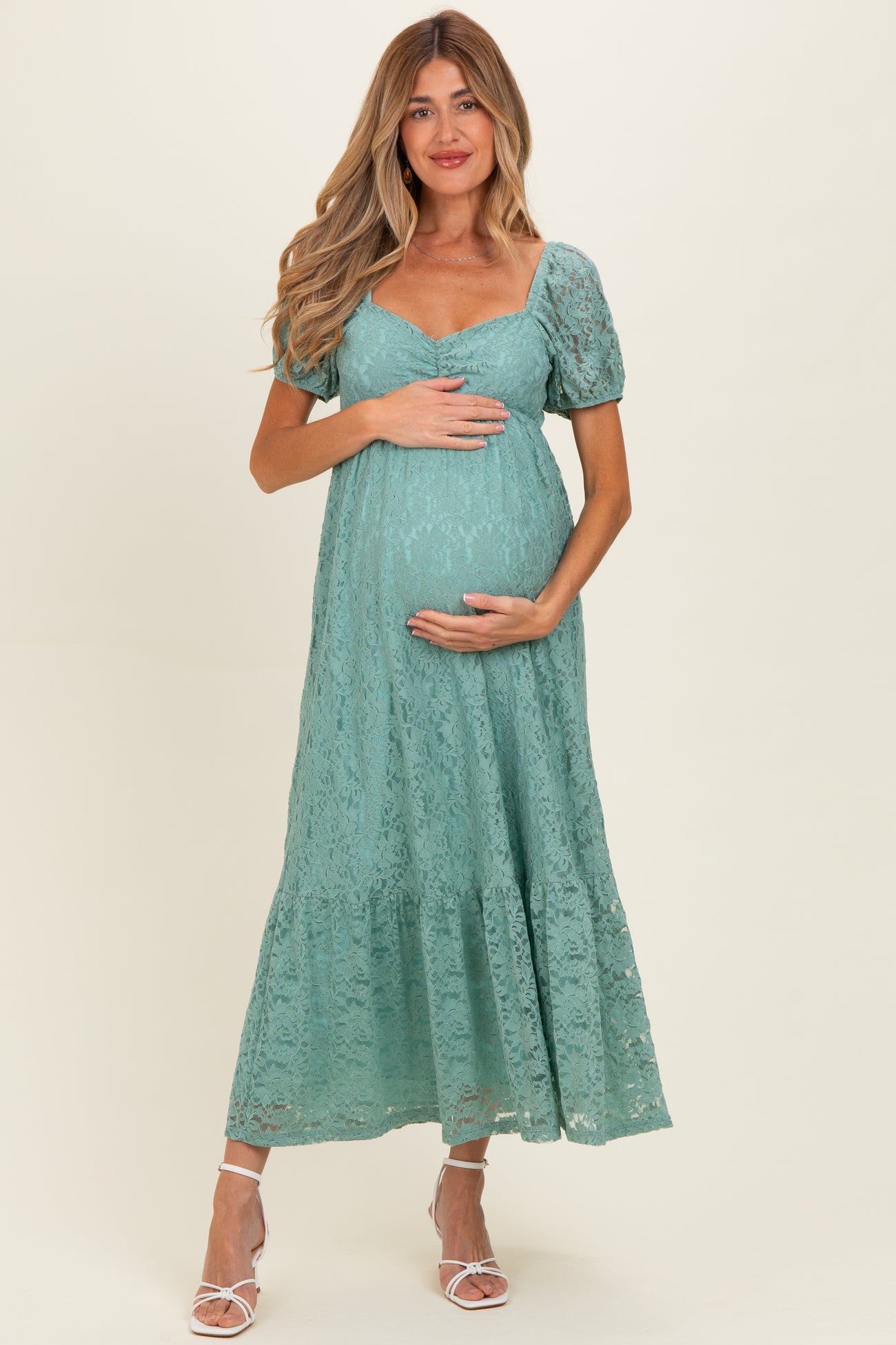 woman wearing a teal lace maternity dress with puff sleeves and a tiered hem, holding her baby bump