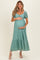 woman wearing a teal lace maternity dress with puff sleeves and a tiered hem, holding her baby bump