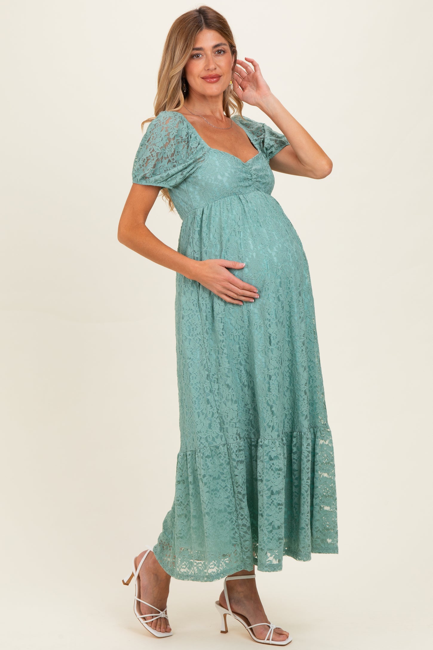 woman wearing a teal lace maternity dress with short puff sleeves and a flowing skirt, holding her baby bump