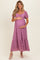 woman wearing a lavender lace maternity dress with puff sleeves and a tiered skirt, holding her baby bump