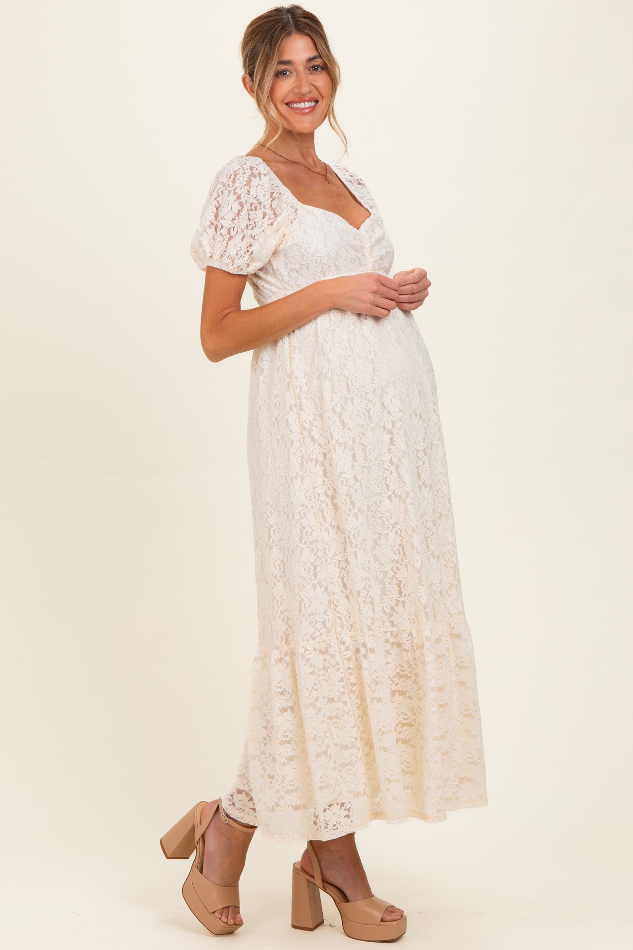 woman wearing a cream lace maternity maxi dress with short puff sleeves and holding her baby bump