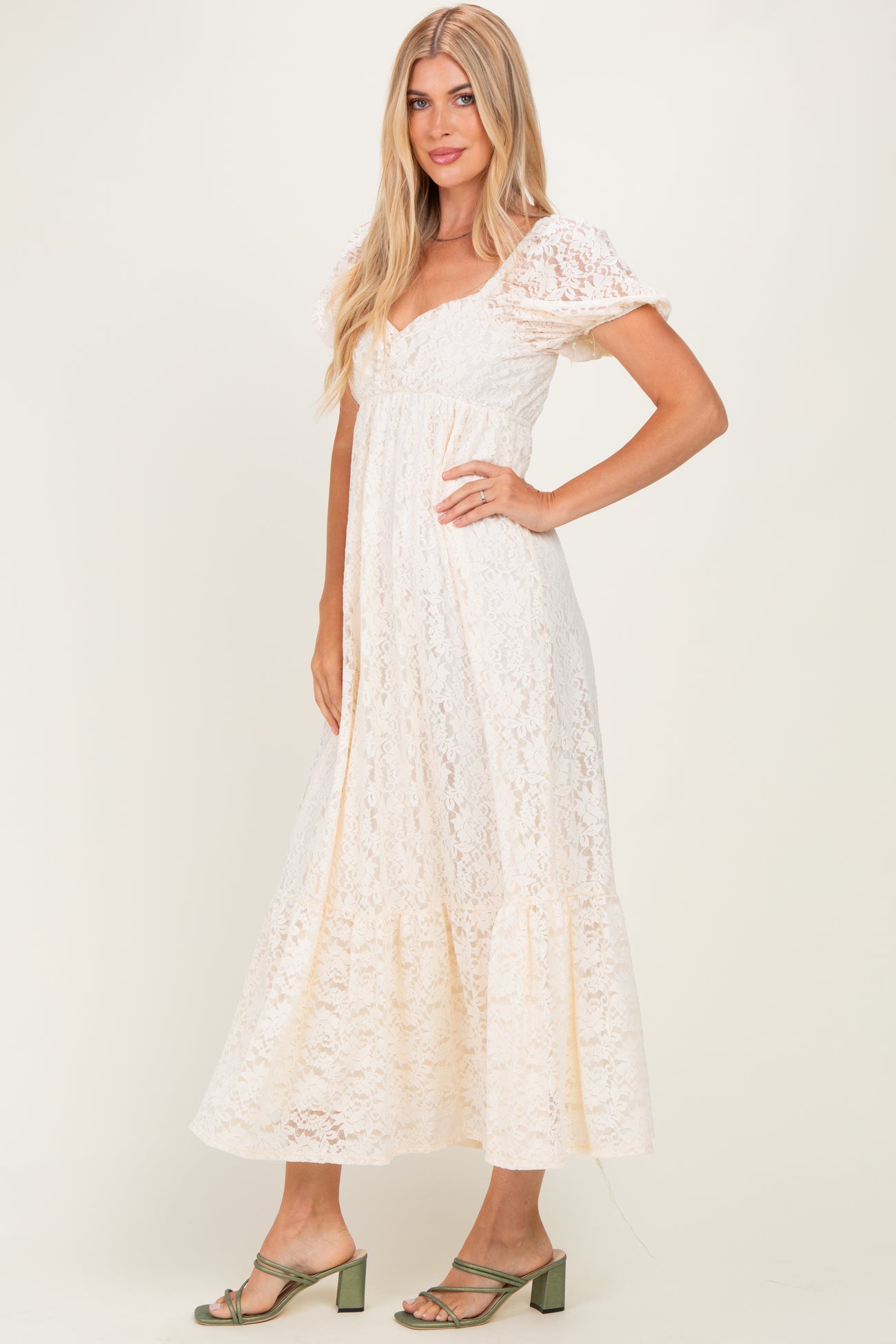 woman wearing a cream lace maxi dress with short puff sleeves and a tiered hem, paired with green block-heeled sandals