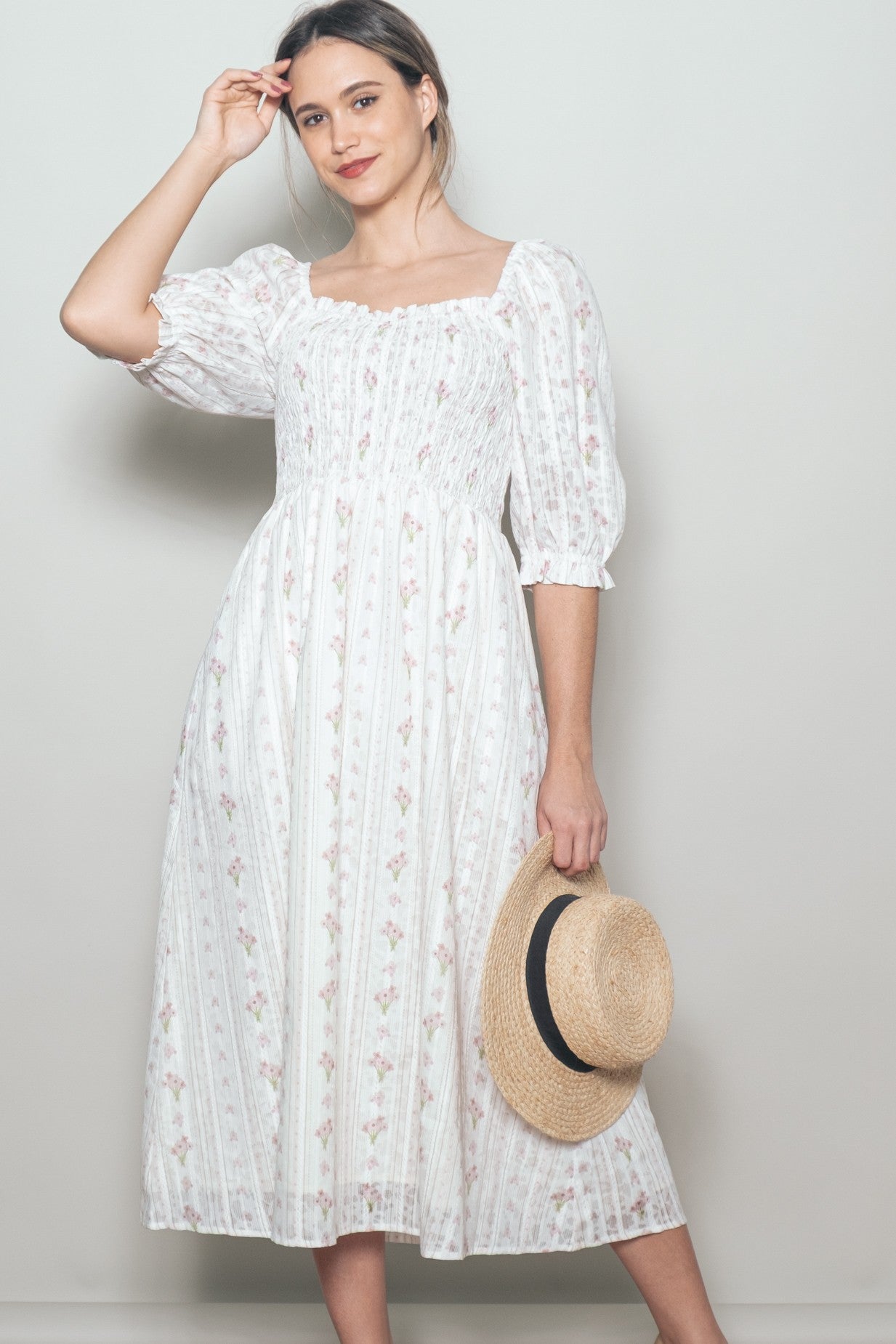 woman wearing a white floral midi dress with puffed sleeves and a square neckline, holding a straw hat