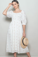 woman wearing a white floral midi dress with puffed sleeves and a square neckline, holding a straw hat
