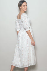 woman wearing a white floral midi dress with puff sleeves and a square neckline, standing sideways against a neutral background